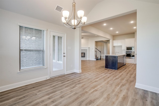 kitchen with light hardwood / wood-style flooring, pendant lighting, a kitchen island with sink, white cabinets, and appliances with stainless steel finishes