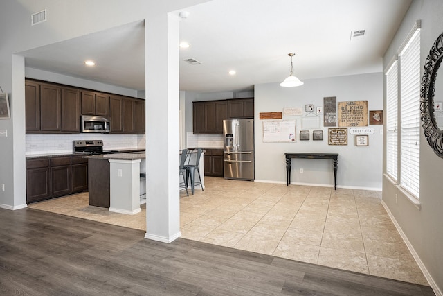 kitchen featuring tasteful backsplash, stainless steel appliances, decorative light fixtures, a kitchen island, and a breakfast bar area