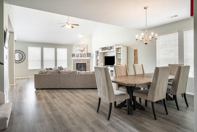 dining room with ceiling fan with notable chandelier, wood-type flooring, a fireplace, and vaulted ceiling