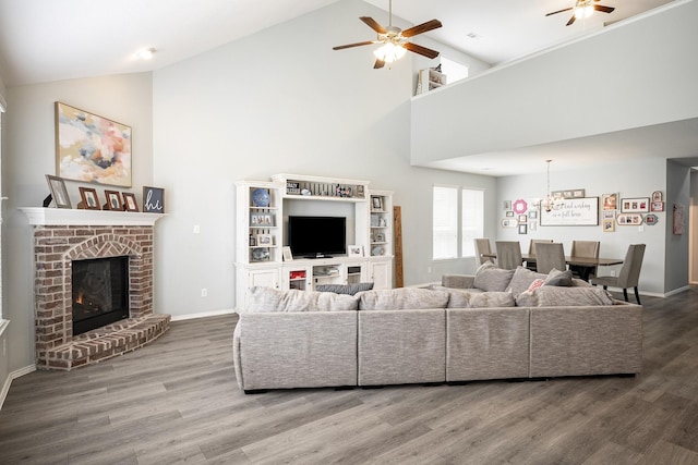 living room featuring a fireplace, ceiling fan with notable chandelier, hardwood / wood-style flooring, and high vaulted ceiling