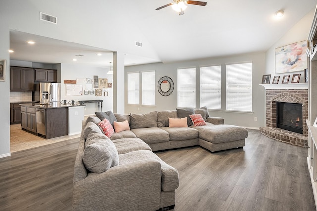 living room featuring ceiling fan, a fireplace, high vaulted ceiling, and light wood-type flooring