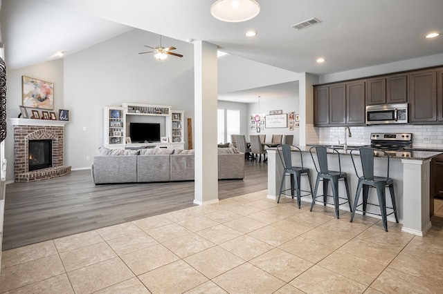 kitchen with appliances with stainless steel finishes, dark brown cabinets, dark stone countertops, a breakfast bar area, and lofted ceiling