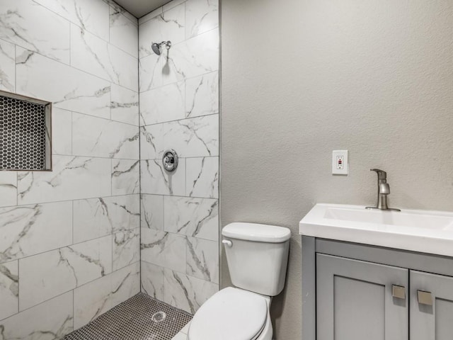 bathroom featuring a tile shower, vanity, and toilet