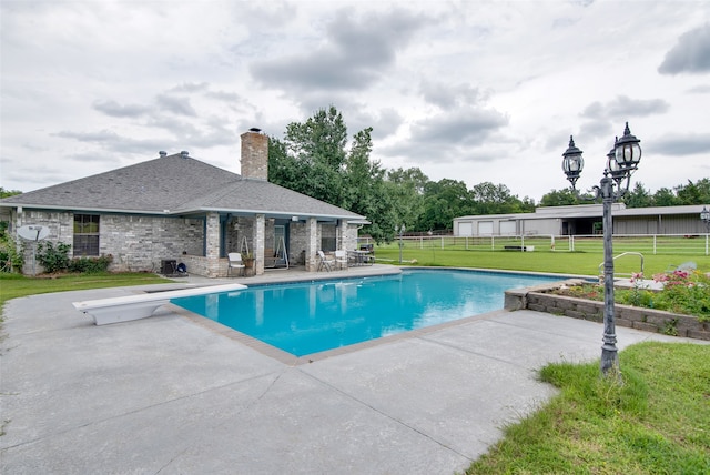 view of swimming pool featuring a yard, a patio area, and a diving board