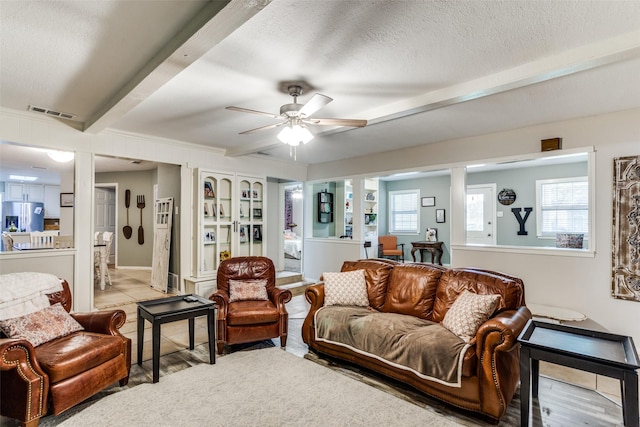 living room featuring ceiling fan, beamed ceiling, and a textured ceiling