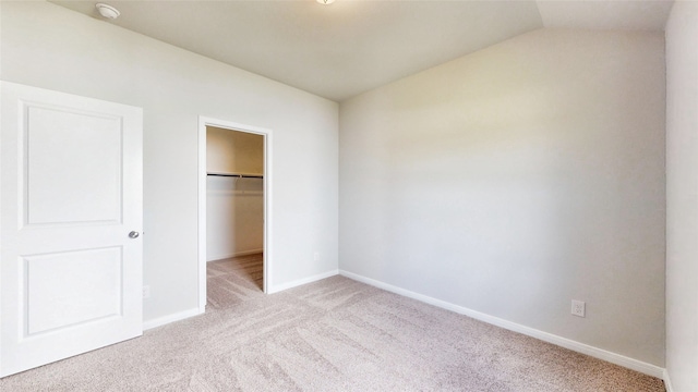 unfurnished bedroom featuring a spacious closet, a closet, light colored carpet, and vaulted ceiling