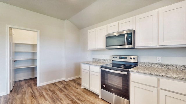 kitchen featuring appliances with stainless steel finishes, lofted ceiling, white cabinetry, and light hardwood / wood-style floors