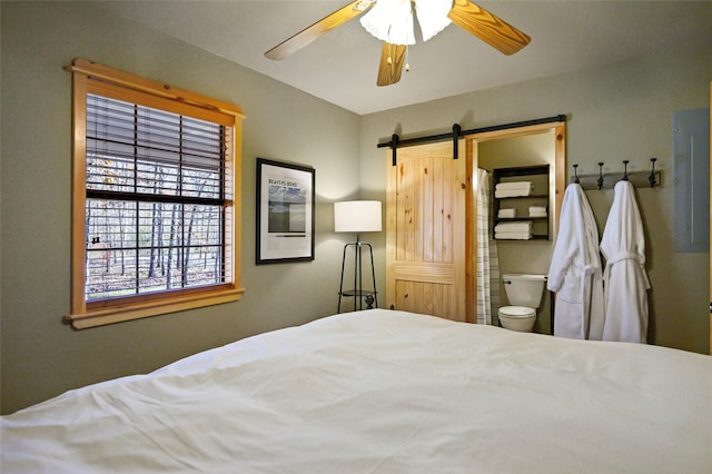 bedroom with a barn door, ensuite bathroom, and ceiling fan