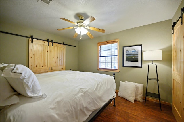 bedroom featuring ceiling fan, a barn door, and dark hardwood / wood-style floors