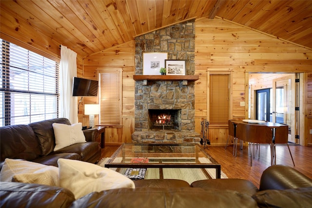 living room with hardwood / wood-style floors, wood walls, a stone fireplace, and vaulted ceiling