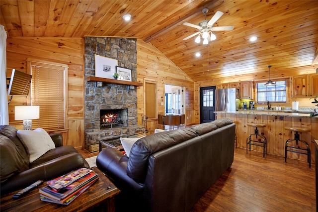 living room with ceiling fan, lofted ceiling with beams, wooden ceiling, hardwood / wood-style floors, and a stone fireplace