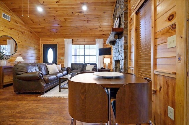 dining area with wood ceiling, wooden walls, dark hardwood / wood-style floors, a stone fireplace, and lofted ceiling