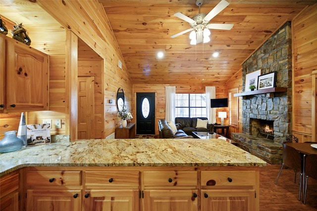 kitchen featuring light stone counters, vaulted ceiling, ceiling fan, wooden walls, and a fireplace