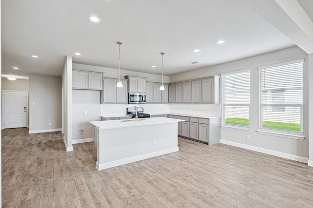 kitchen with sink, gray cabinets, a kitchen island with sink, decorative light fixtures, and light wood-type flooring