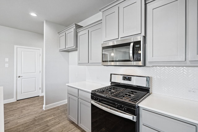 kitchen with gray cabinets, decorative backsplash, stainless steel appliances, and light wood-type flooring