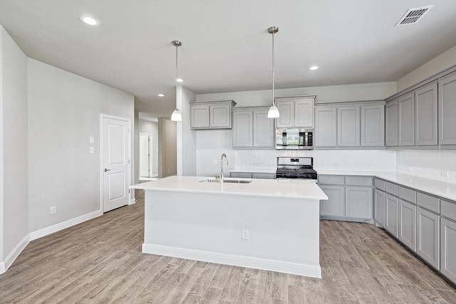 kitchen with appliances with stainless steel finishes, sink, light wood-type flooring, and pendant lighting