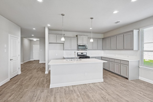 kitchen featuring appliances with stainless steel finishes, sink, light wood-type flooring, hanging light fixtures, and a center island with sink