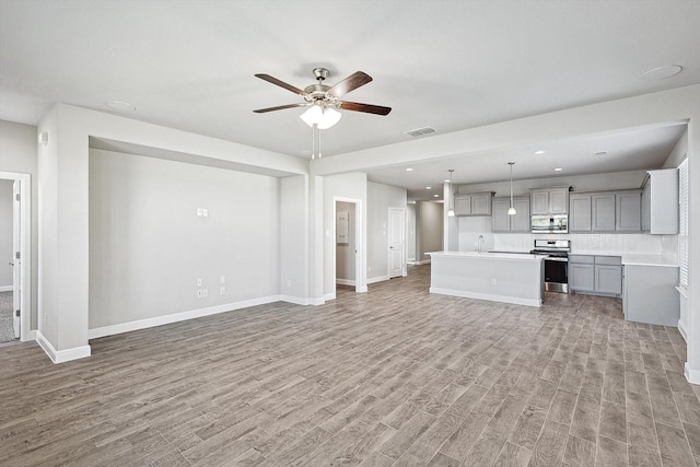 unfurnished living room featuring hardwood / wood-style floors, sink, and ceiling fan