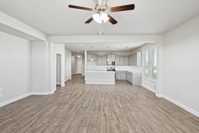 unfurnished living room with sink, light wood-type flooring, and ceiling fan