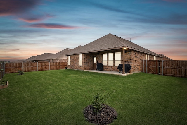 back house at dusk featuring a yard and a patio