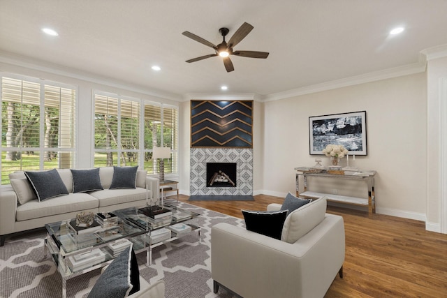 living room with a tiled fireplace, crown molding, ceiling fan, and hardwood / wood-style flooring