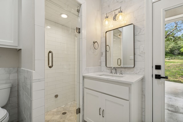 bathroom featuring vanity, toilet, a shower with door, and tile walls