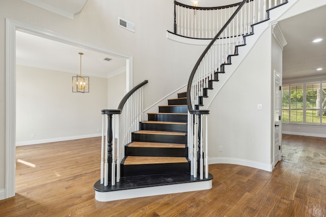 staircase featuring crown molding, hardwood / wood-style floors, and a chandelier