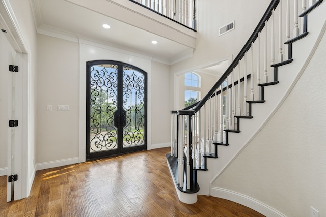 foyer featuring french doors, a towering ceiling, hardwood / wood-style floors, and ornamental molding