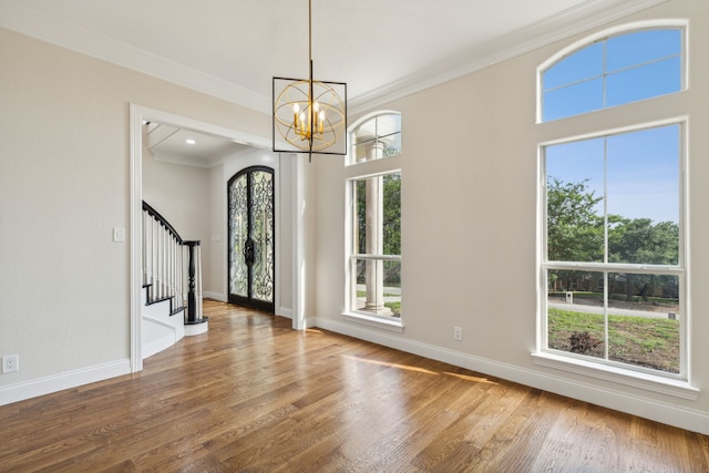 foyer with wood-type flooring, an inviting chandelier, french doors, and crown molding