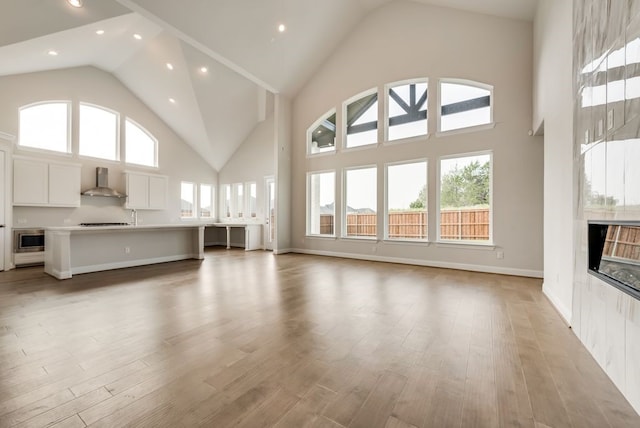 unfurnished living room with light wood-type flooring, a towering ceiling, and a fireplace