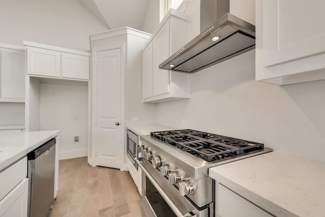 kitchen with appliances with stainless steel finishes, wall chimney exhaust hood, white cabinetry, and light hardwood / wood-style flooring