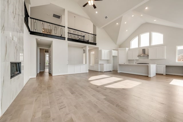 unfurnished living room with a wealth of natural light, a tile fireplace, a towering ceiling, and light wood-type flooring