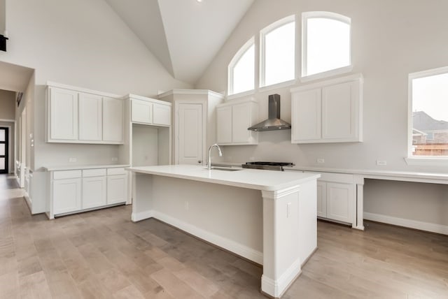 kitchen with an island with sink, white cabinets, and wall chimney range hood