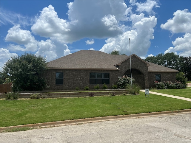 ranch-style home with brick siding, a front yard, and a shingled roof