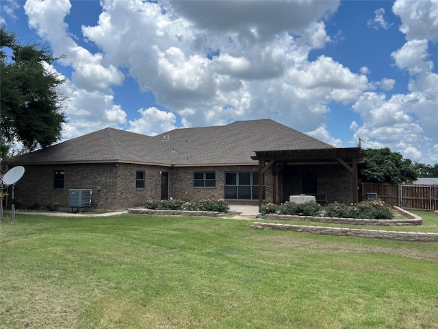 rear view of property with fence, central AC, a shingled roof, a lawn, and brick siding