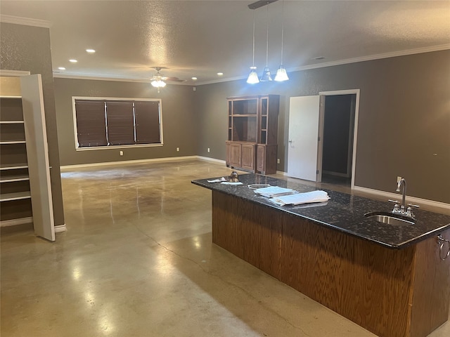 kitchen with hanging light fixtures, ceiling fan, an island with sink, crown molding, and sink