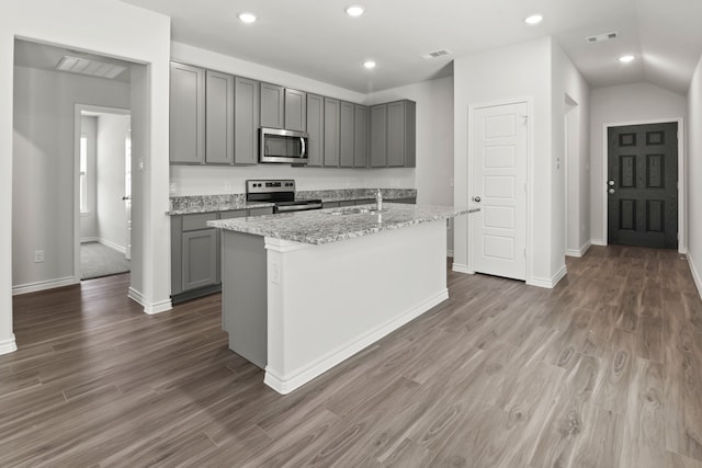 kitchen with dark wood-type flooring, a center island with sink, gray cabinets, and appliances with stainless steel finishes