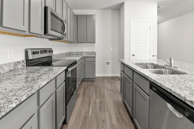 kitchen featuring light stone countertops, wood-type flooring, gray cabinetry, sink, and appliances with stainless steel finishes