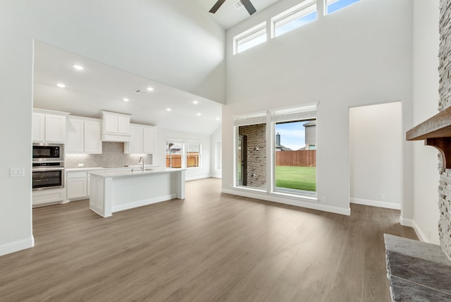 unfurnished living room featuring light hardwood / wood-style floors, a high ceiling, and ceiling fan