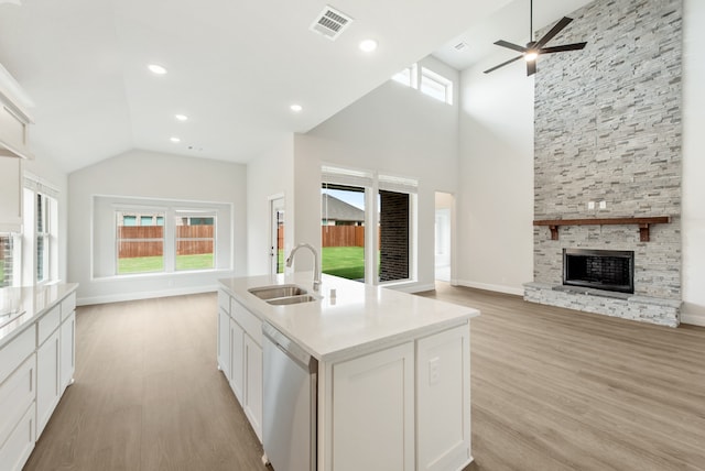 kitchen with light wood-type flooring, stainless steel dishwasher, an island with sink, sink, and a fireplace