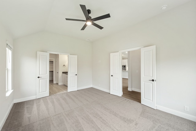 unfurnished bedroom with ceiling fan, vaulted ceiling, connected bathroom, and light carpet