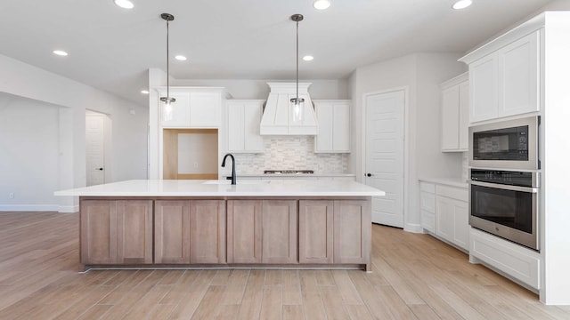 kitchen featuring a center island with sink, stainless steel oven, pendant lighting, and white cabinets