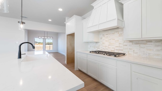 kitchen featuring custom exhaust hood, white cabinetry, hardwood / wood-style flooring, stainless steel gas stovetop, and pendant lighting