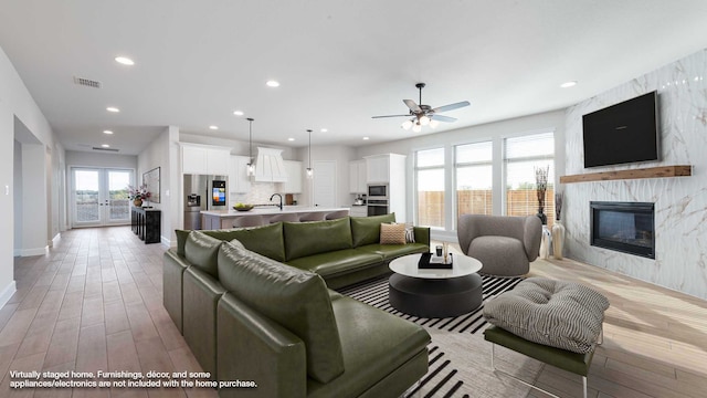 living room featuring ceiling fan, a high end fireplace, light hardwood / wood-style flooring, french doors, and sink