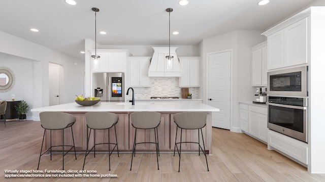 kitchen featuring hanging light fixtures, a center island with sink, appliances with stainless steel finishes, white cabinetry, and light wood-type flooring