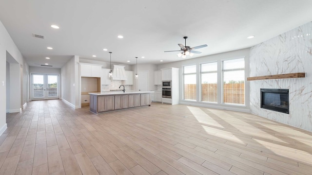 unfurnished living room featuring french doors, sink, a fireplace, light hardwood / wood-style floors, and ceiling fan