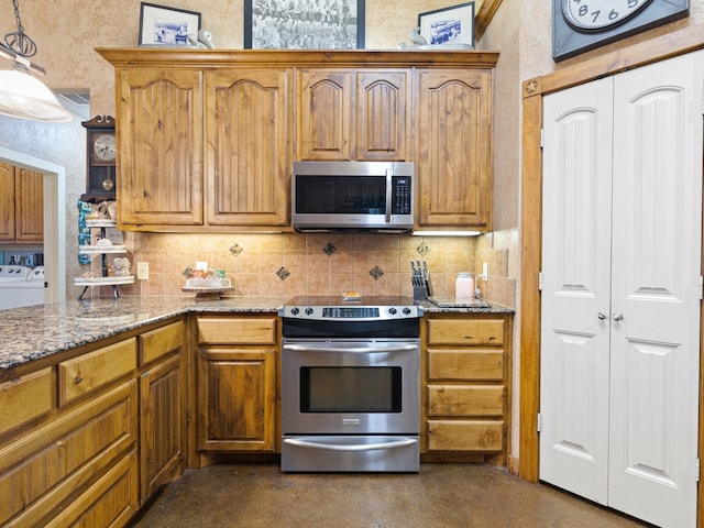 kitchen with decorative light fixtures, appliances with stainless steel finishes, washing machine and clothes dryer, stone counters, and backsplash