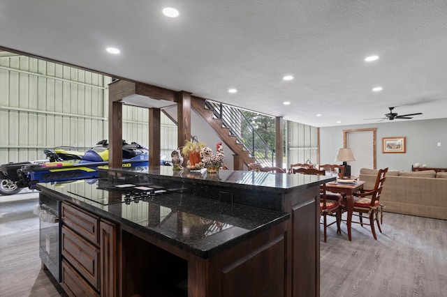 kitchen with ceiling fan, dark stone countertops, a kitchen island, and light hardwood / wood-style flooring