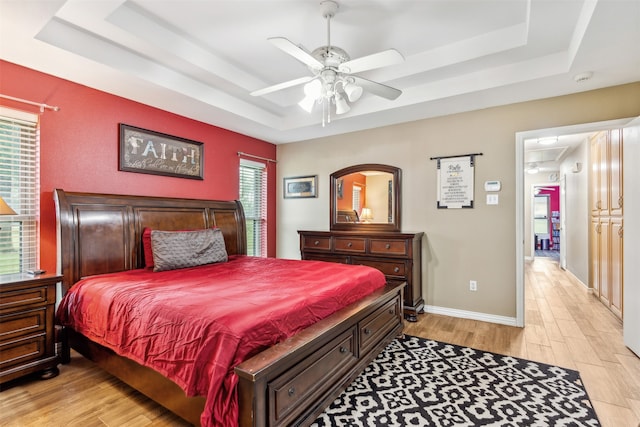 bedroom featuring ceiling fan, light hardwood / wood-style flooring, and a tray ceiling