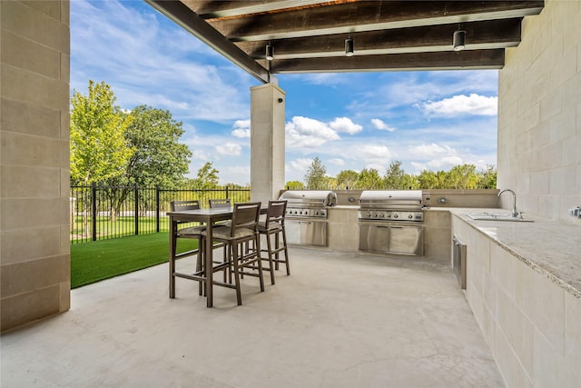 view of patio with a grill, fence, an outdoor kitchen, and a sink